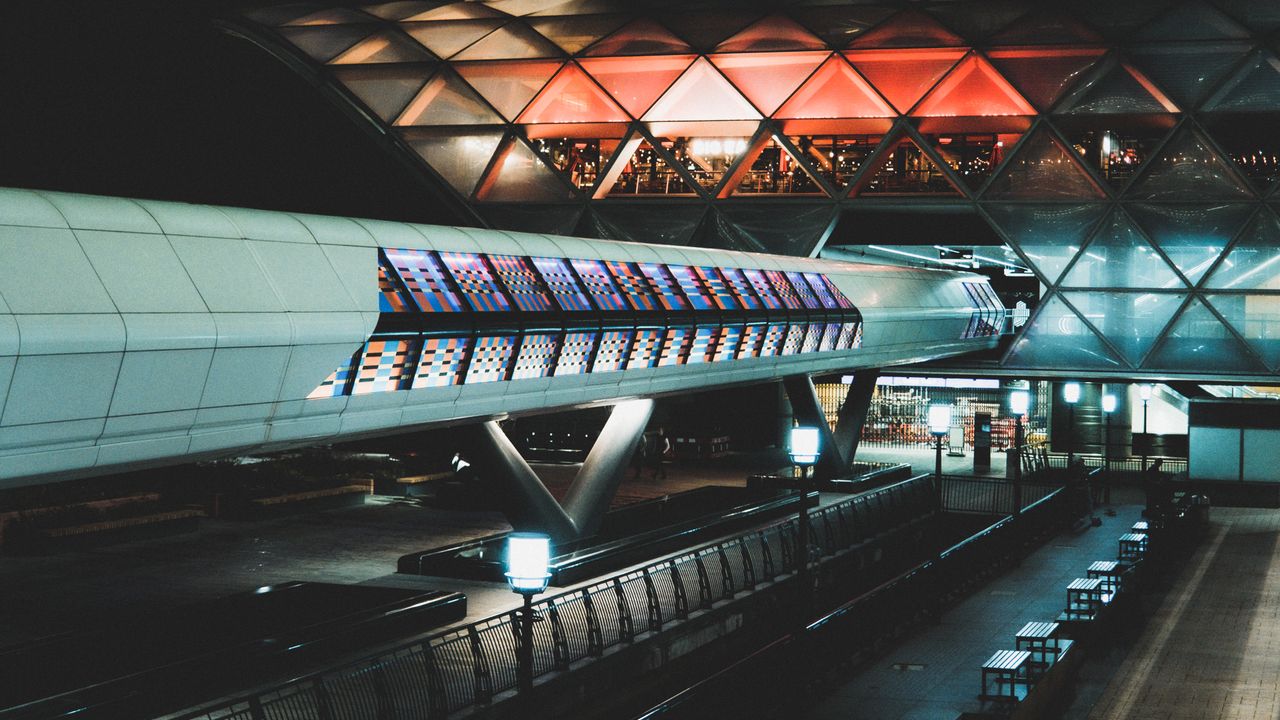 A terminal concourse at night under a glass canopy, the walkway lit above
